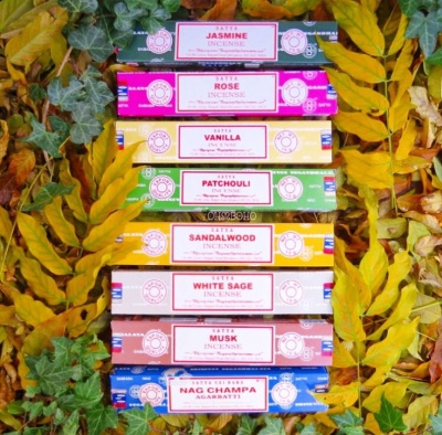 Caixas coloridas de incenso empilhadas entre folhas verdes e amarelas