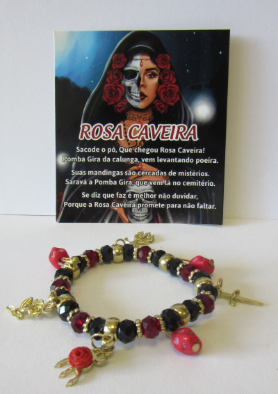 Pulseira vermelha, preta e dourada com pendentes dourados e cartão com imagem de figura feminina metade caveira e texto ao fundo.