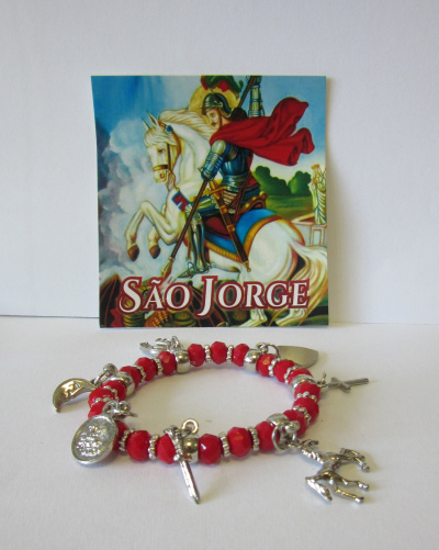 Pulseira vermelha com pendentes prateados e imagem de São Jorge ao fundo