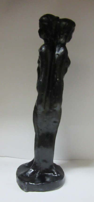 Escultura preta de duas figuras femininas unidas pelas costas numa base circular