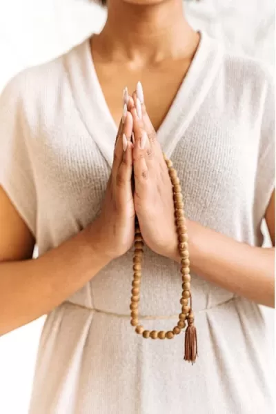 Pessoa segurando rosário de contas de madeira com tassel entre as mãos em oração