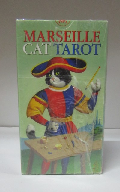 Caixa do jogo MARSEILLE CAT TAROT com gato vestido colorido e mesa de madeira com objetos