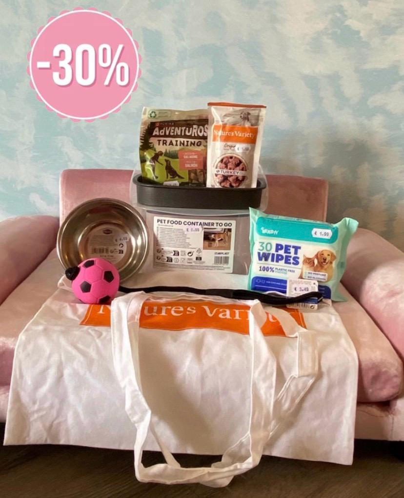 Pack Parque Produtos para cães com saco, bola, taça metálica, recipiente plástico, snacks e toalhitas numa cadeira rosa