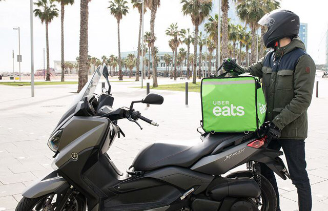 Motocicleta preta com mochila de entrega Uber Eats verde e homem com capacete ao lado