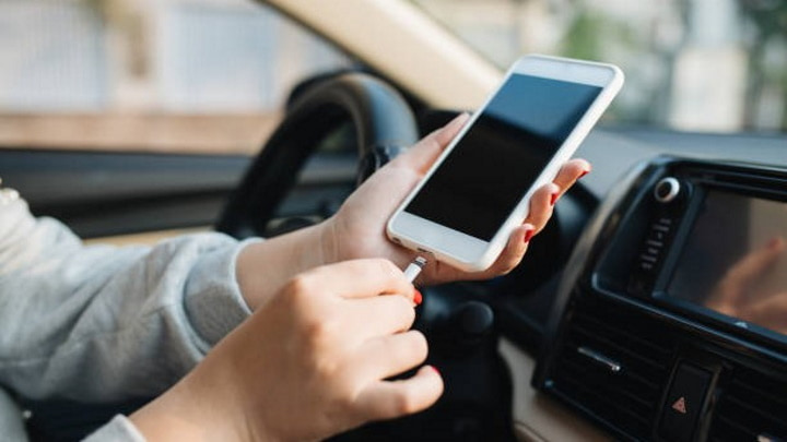 Pessoa a conectar cabo USB em telemóvel dentro de carro com consola visível