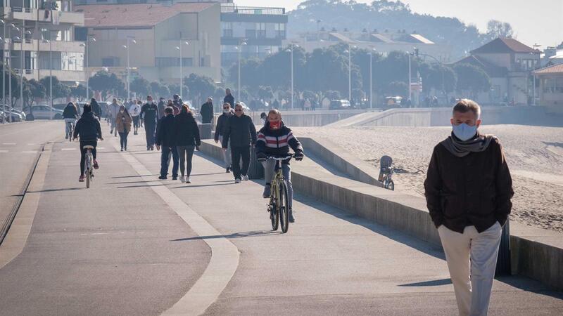 Pessoa a caminhar e andar de bicicleta numa passadeira perto da praia com edifícios ao fundo
