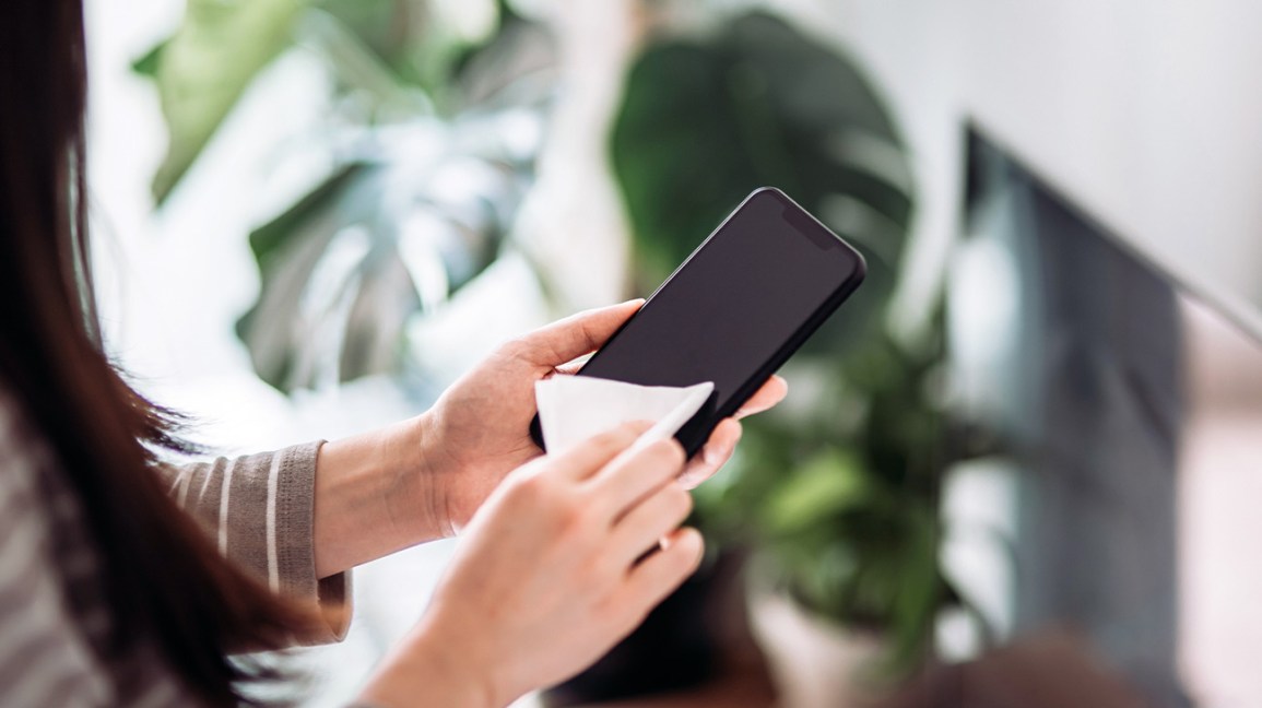 Pessoa a limpar a tela de um smartphone preto com um pano branco