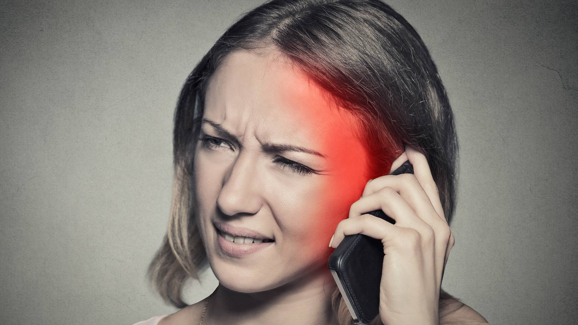 Mulher com dor segurando telemóvel junto à cabeça com luz vermelha ao lado da face
