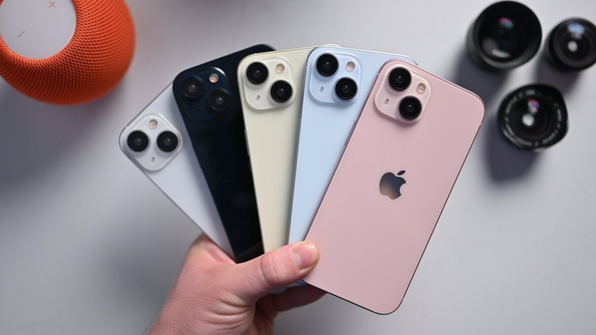 Cinco iPhones de várias cores segurados por uma mão sobre fundo branco