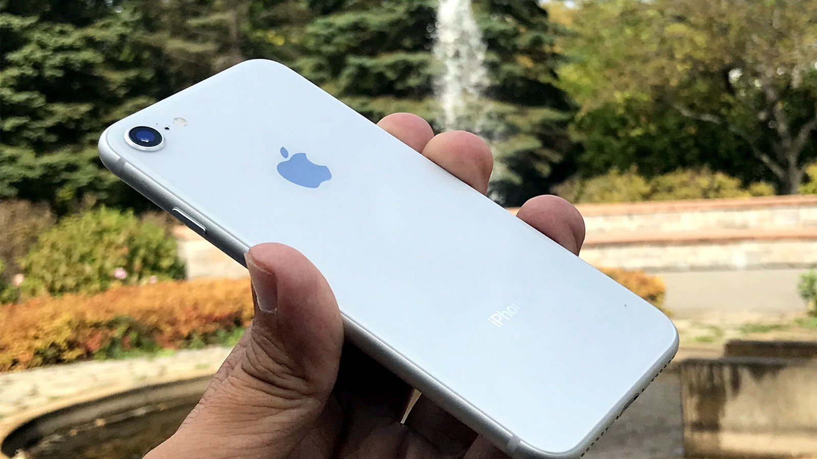 Smartphone iPhone branco segurado com fundo de jardim e fonte