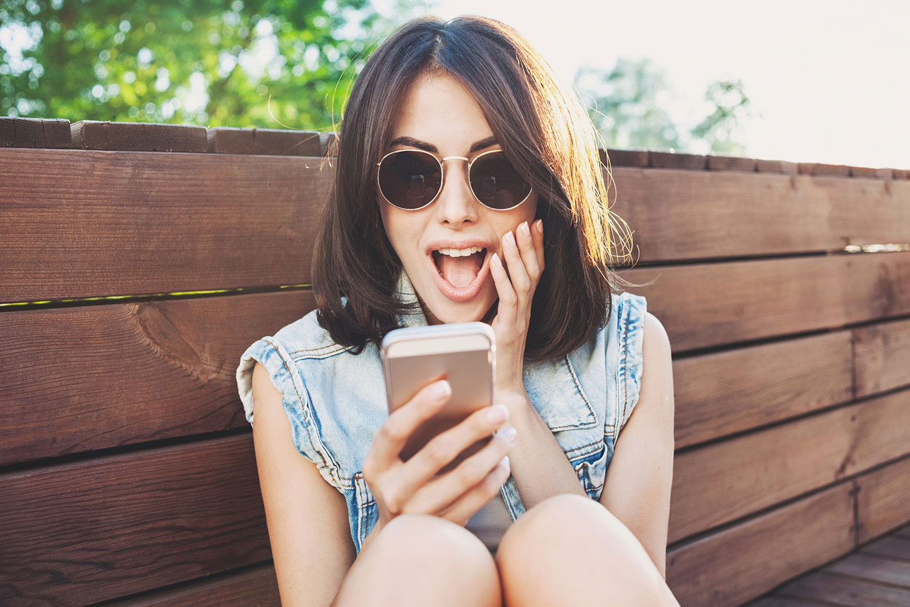 Mulher com óculos de sol e colete jeans usando telemóvel junto a cerca de madeira