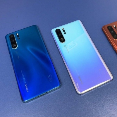 Três telemóveis Huawei coloridos numa superfície azul