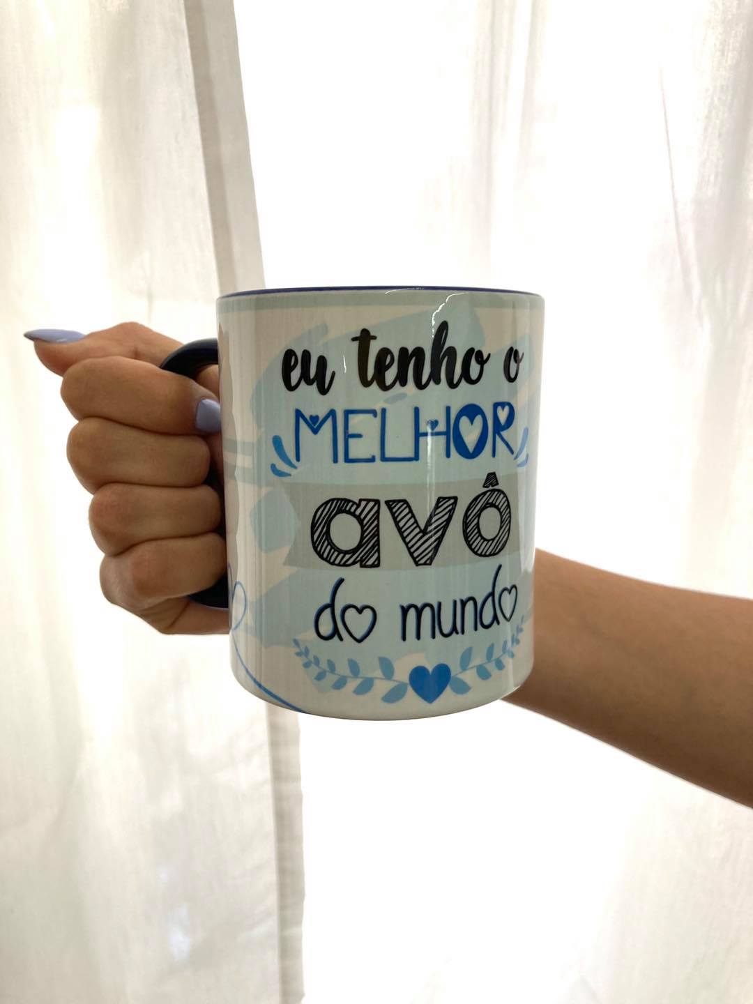 Caneca eu tenho o melhor avô Caneca branca com texto 'eu tenho o MELHOR avô do mundo' segurada por mão com unhas azul claro