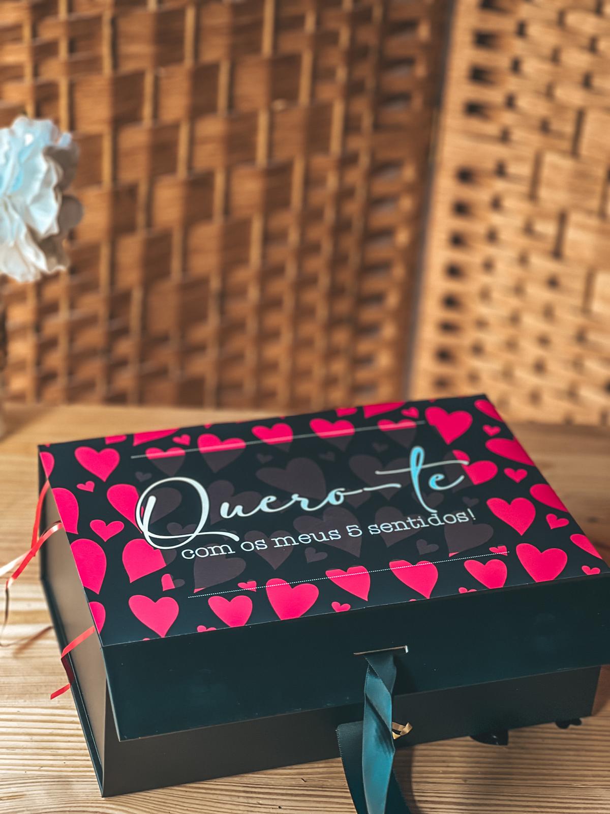 Caixa 5 sentidos Caixa de presente preta com corações vermelhos e texto Quero-te com os meus 5 sentidos! numa mesa de madeira.