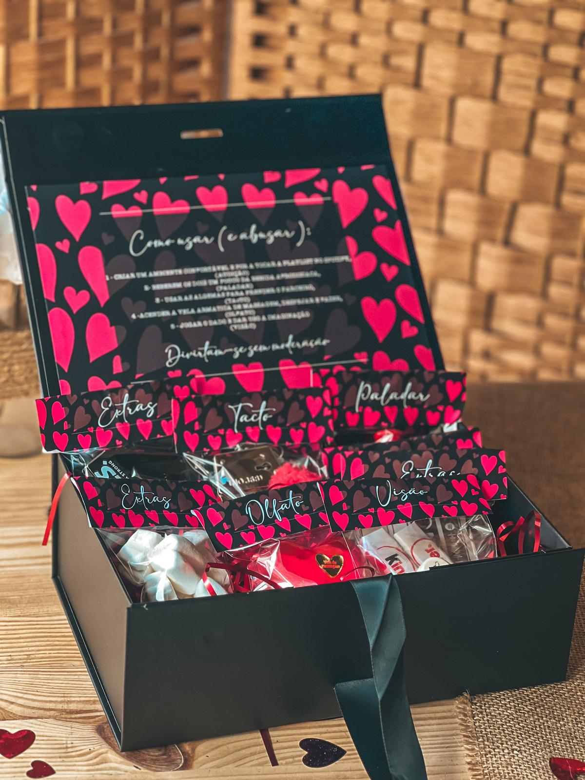 Caixa 5 sentidos Caixa preta com pacotes pequenos decorados com corações vermelhos e etiquetas com sentidos