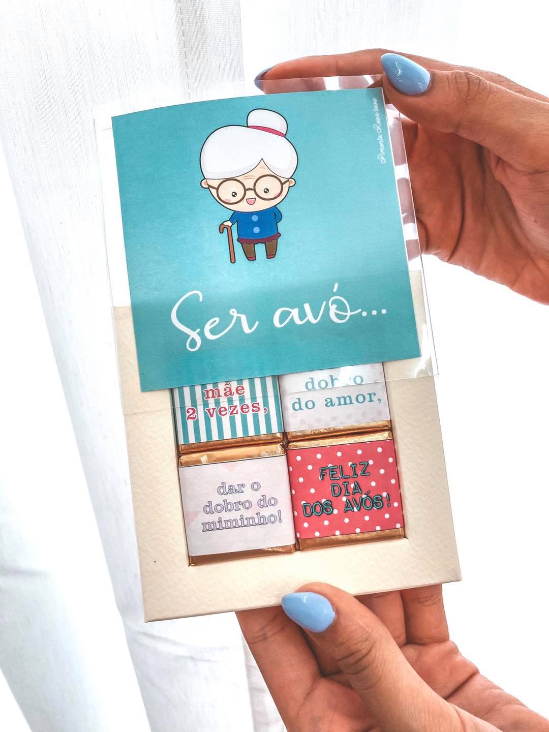 conjunto avó 2 Caixa de chocolates com mensagens de feliz dia dos avós segurada por mãos femininas com unhas azuis.