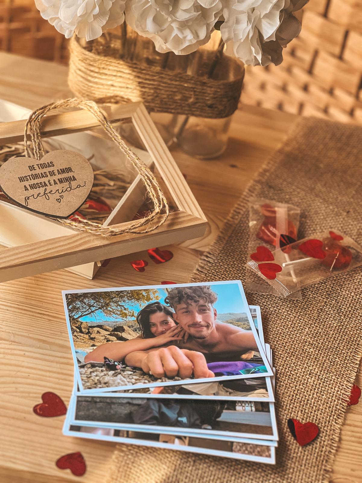 Caixinha com fotos e iman. Fotografias de casal, cartão em forma de coração com mensagem, pirulitos vermelhos sobre mesa de madeira