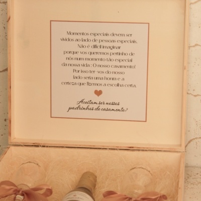 Caixa de madeira com champanhe, dois copos com laços cor de rosa e mensagem em português para padrinhos de casamento
