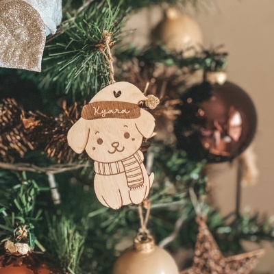 Enfeite natalício em madeira de cão com texto Kyara num ramo de árvore de Natal com bolas coloridas.