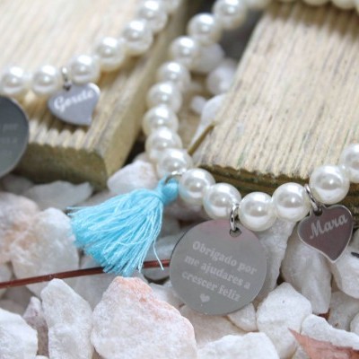 Pulseiras de pérolas brancas com medalha redonda gravada e pendentes em fio azul sobre pedras brancas
