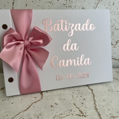 Álbum branco com laço rosa e texto metálico cor de rosa 'Batizado da Camila 09-06-2024'
