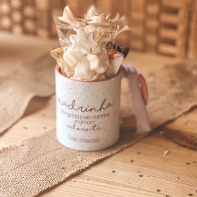 Caneca decorativa branca com texto em português e embalagem com enfeites sobre mesa de madeira.