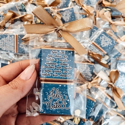 Chocolate embrulhado para presente com mensagem de Natal em português, fita castanha e fundo azul com estrelas brancas.