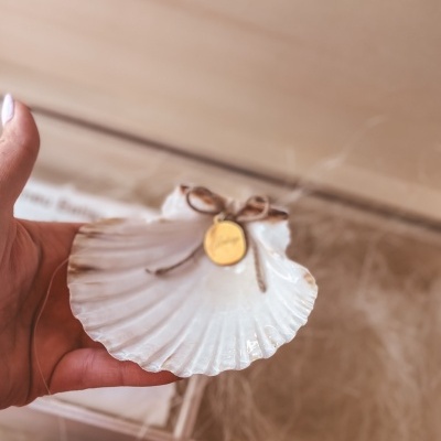Mão segurando uma concha branca com fio e medalha dourada