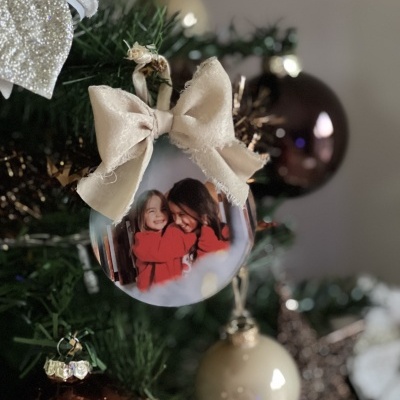 Bola de Natal transparente com fotografia e laço bege numa árvore de Natal