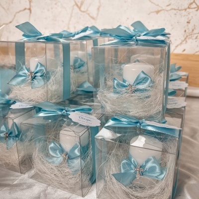Velas decorativas brancas em caixas transparentes com laços azuis e cruzes prateadas