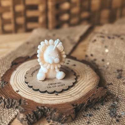 Vela decorativa branca em forma de leão sobre fatia de madeira com texto Afonso 06-07-2027 e fundo de juta