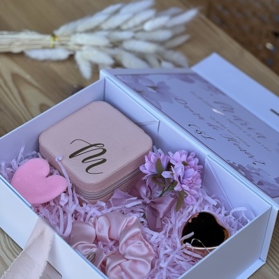 Caixa branca com acessórios de cor rosa e lilás e flores artificiais