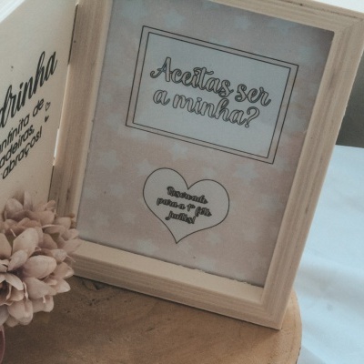 Livro de madeira aberto com texto e flores secas, ao lado de quadro com texto em português.