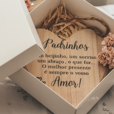 Placa de madeira em forma de coração com texto em caixa branca aberta junto a flores secas cor de rosa