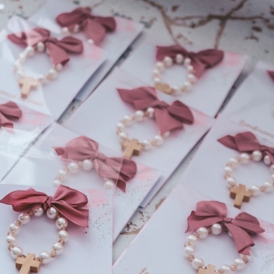 Brincos de pérolas com cruz dourada e laço rosa em cartões de batizado