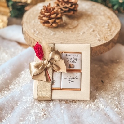 Caixa de chocolates embrulhada com fita dourada e texto de Natal em português.