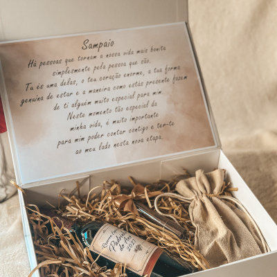 Caixa branca com garrafa de vinho, saquinho de tecido e texto impresso interno