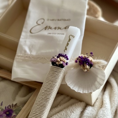 Conjunto de vela decorada, concha com flores secas e saco branco com texto para batismo em caixa de madeira.