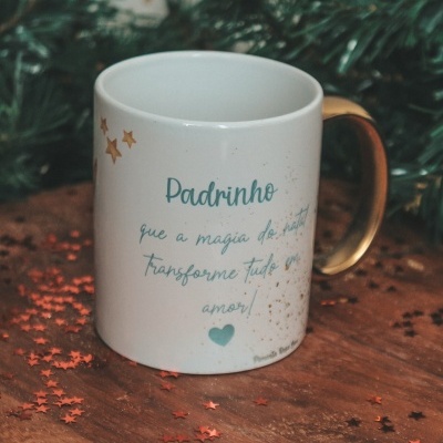 Caneca branca com pega dourada e texto azul em fundo de madeira e decoração natalícia