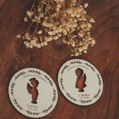 Dois enfeites circulares em madeira com anjos e textos, sobre madeira escura com raminhos secos