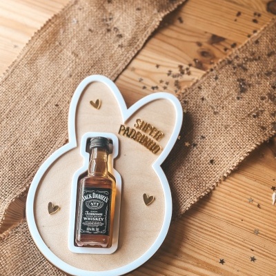 Garrafa pequena de whiskey Jack Daniels numa base de madeira em forma de coelho com decoração em juta