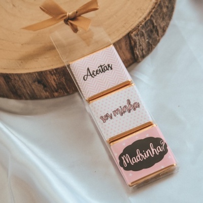 Chocolates decorativos com rótulos variados em embalagem transparente sobre tecido branco e base de madeira