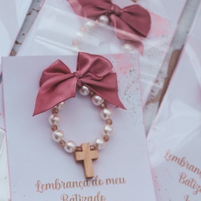 Pulseira perolada com cruz de madeira e laço rosa em cartão comemorativo de batizado