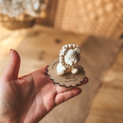 Miniatura de leão branco sobre base de cartão com texto em mão humana.