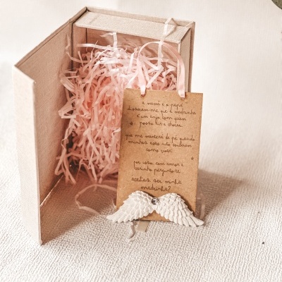 Caixa de presente em tecido bege com cartão kraft com texto manuscrito e asas brancas decorativas