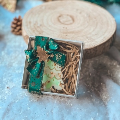 Caixa de presente com sabonete em forma de árvore de Natal decorada com laço verde e fundo de neve e madeira