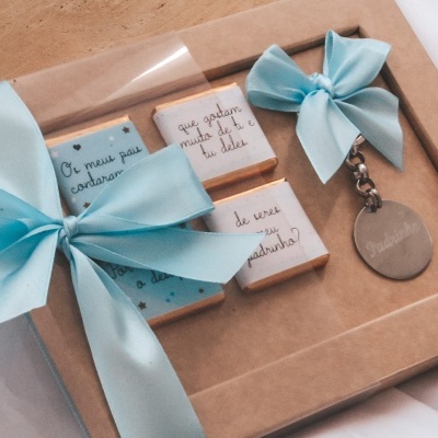 Conjunto de presentes em caixa com fita azul clara, incluindo peças decorativas e porta-chaves prateado.