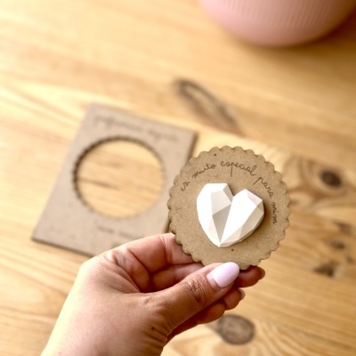 Mão a segurar cartão redondo de papel castanho com coração branco 3D e frase escrita
