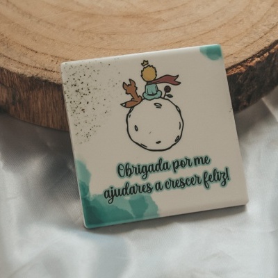 Quadrado de cerâmica com ilustração infantil e texto em português sobre tecido branco
