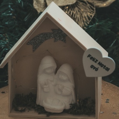 Presépio natalício branco em casa de madeira clara com estrela glitter e coração com texto 'Feliz Natal evd'